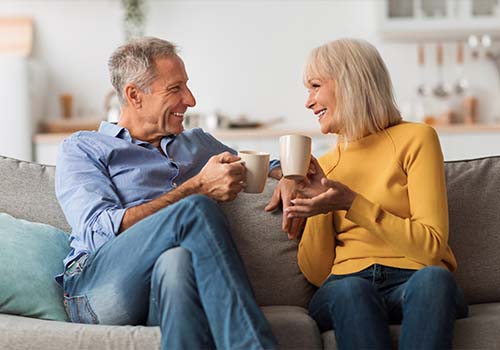 Cheerful Elderly Couple Drinking Tea And Talking On Couch