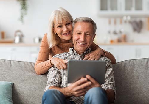 Cheerful Retired Couple On Couch Using Laptop