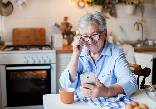 Senior using a mobile phone in their kitchen.