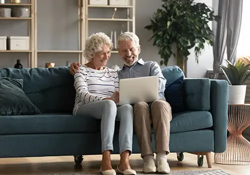 An elderly couple sitting on the couch researching social security spousal benefits.