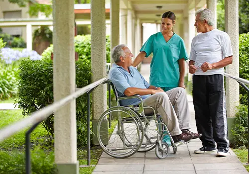 Two Senior Citizens Talking To A Nurse In Nursing Home Garden