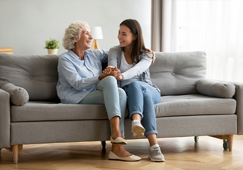 Happy Adult Grandmother And Granddaughter Talking On Sofa