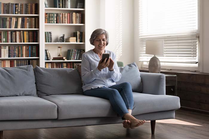 A retired elderly woman sitting on a couch using her cellphone.
