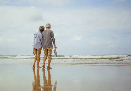 Senior Couple Walking On The Beach Holding Hands
