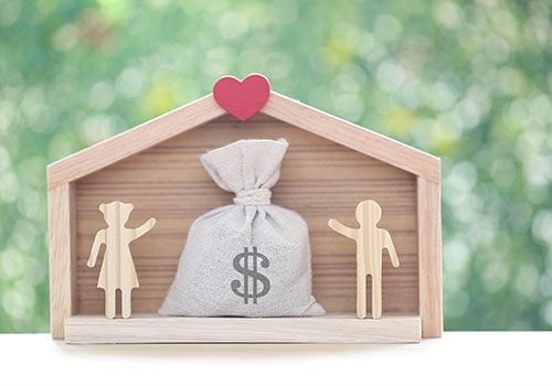 Wooden figurines of a man and woman inside a house next to a bag of money.