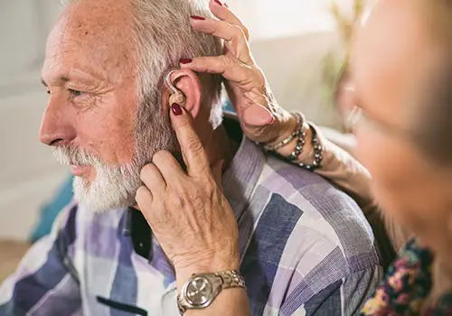 An elderly man has help fitting his hearing aid.