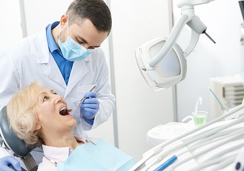 A dentist inspects an elderly woman's teeth.