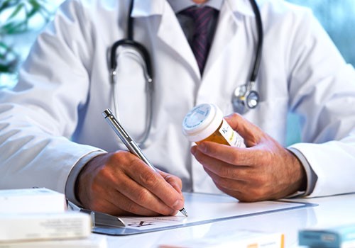 A doctor looking at a pill bottle while writing a prescription.