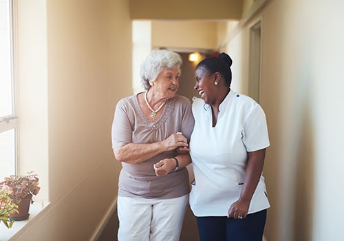 A nurse and old woman laughing while with linked arms.