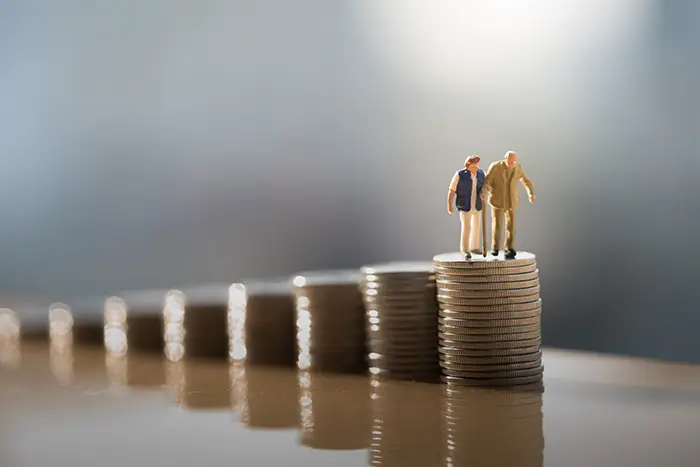 Miniature figurines of an old couple standing on top of a coin stack retirement planning concept.