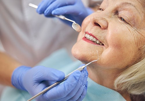 A smiling elderly woman having her teeth inspected.