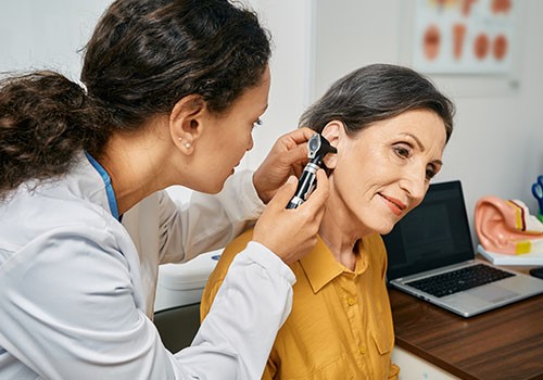 A woman has her ear inspected by a doctor.