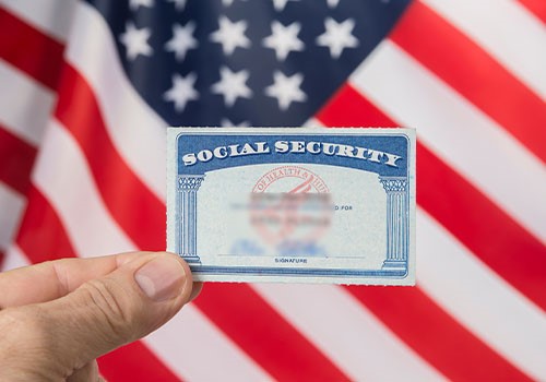 A Social Security card with the start spangled banner flag in the background.