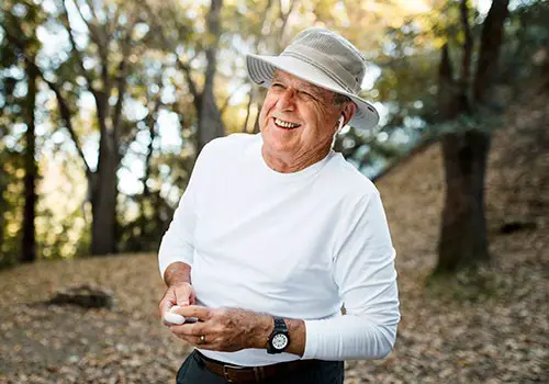 An elderly man wearing hat whilst standing in a forest.