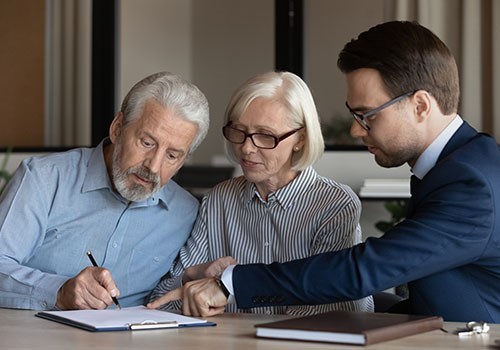 An elderly couple signing documents in front of a lawyer.