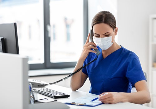 A nurse with a mask on talks on the phone.