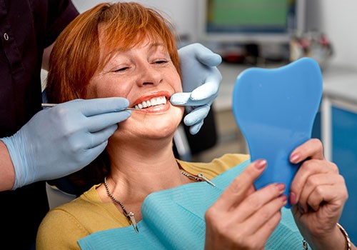 A lady smiles as she looks at her new dentures in the mirror.