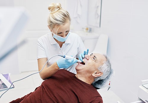 A female dentist works on an elderly man's teeth.
