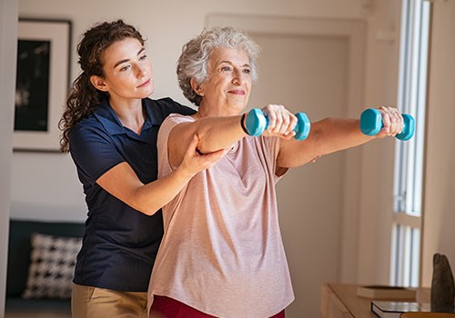 An elderly lady is lifting small dumbells during a physical therapy session.