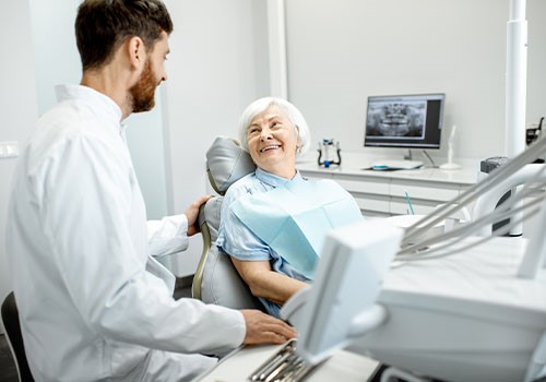 An elderly lady in the dentists chair talking to her dentist.