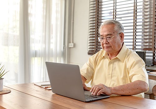 An elderly man sitting at a desk on his laptop computer.