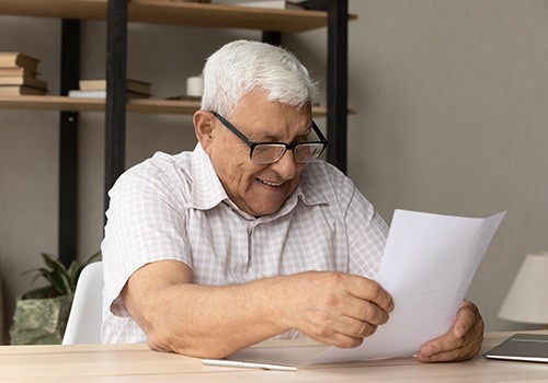 An elderly man is reading a letter and smiling.