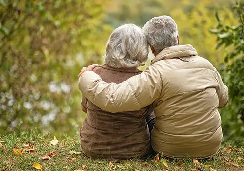 A view from behind of an elderly couple sitting on the grass hugging.