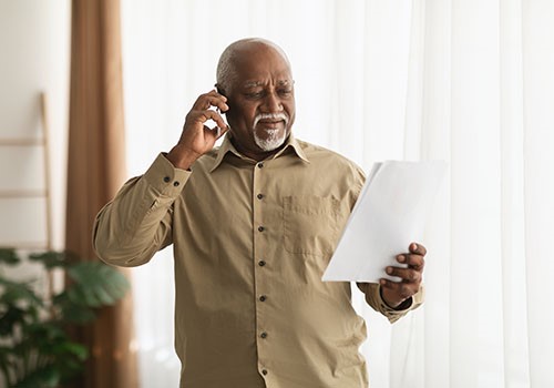 An elderly man on the phone while looking at paperwork.