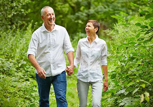 A middle aged couple holding hands and walking through a field.