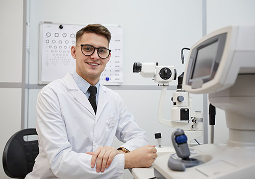 Closeup of male Ophthamologist smiling at the camera while posing in a room with optic testing equipment.