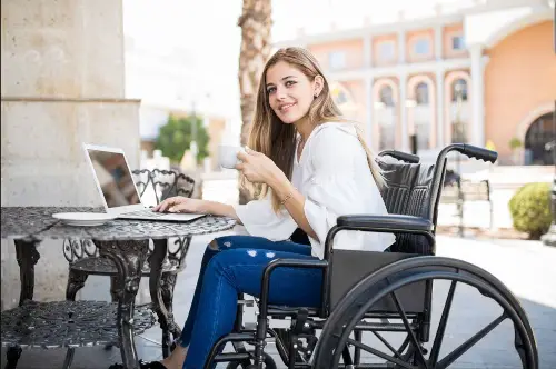 A young disabled woman in a wheelchair working at her laptop.