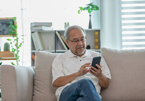 Elderly man sitting on a couch while using his mobile phone.