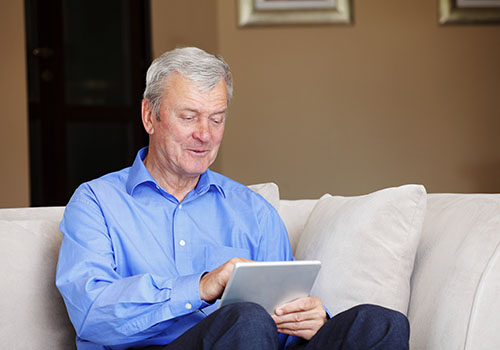 Healthy and smiling senior man sitting on a couch while using his tablet.