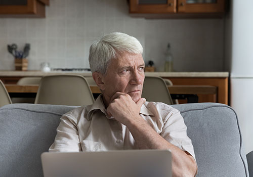 A pensive stressed elderly man sitting on a couch after receiving bad news.