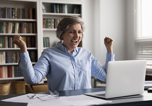 Smiling elderly woman using laptop after receiving good news.