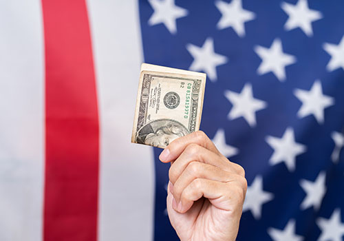Hand holding American Dollars with the American flag in the background.