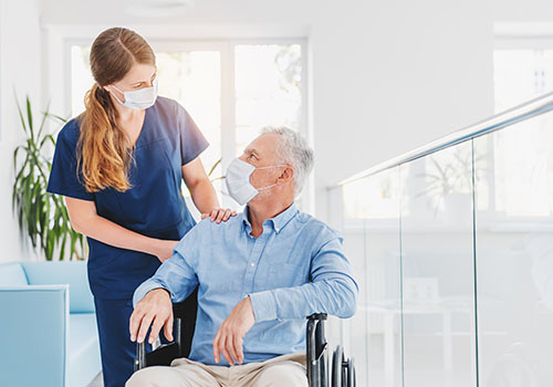 A young female nurse explaining information to an elderly man in a wheelchair in a hospital setting.