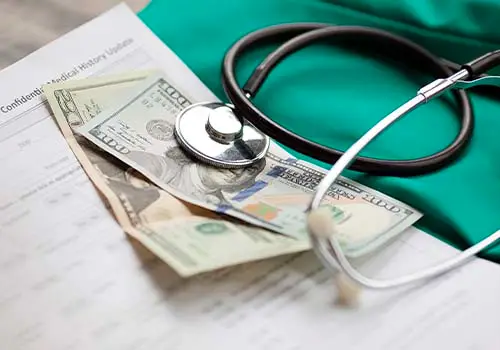 A stethoscope on top of money and a medical record form.