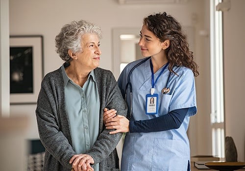 An elderly woman walking arm-in-arm with her nurse.