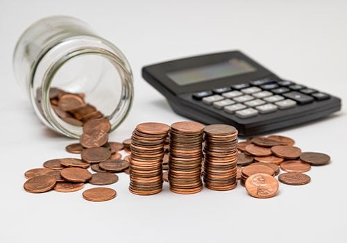 A spilled jar of pennies next to a calculator.