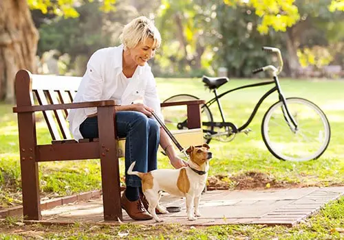 A woman sitting on a park bench next to her dog and bicycle.