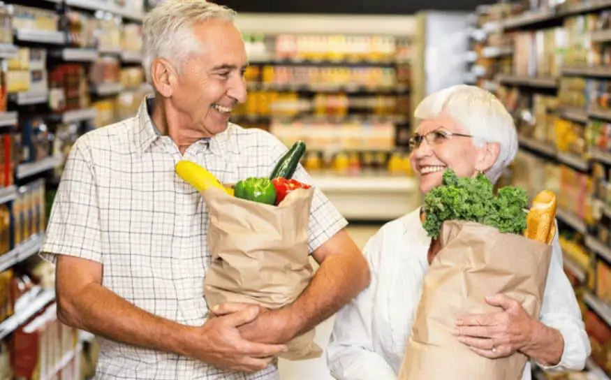 An elderly man and woman holding groceries they paid for using a Medicare Advantage Plan Grocery Benefit.