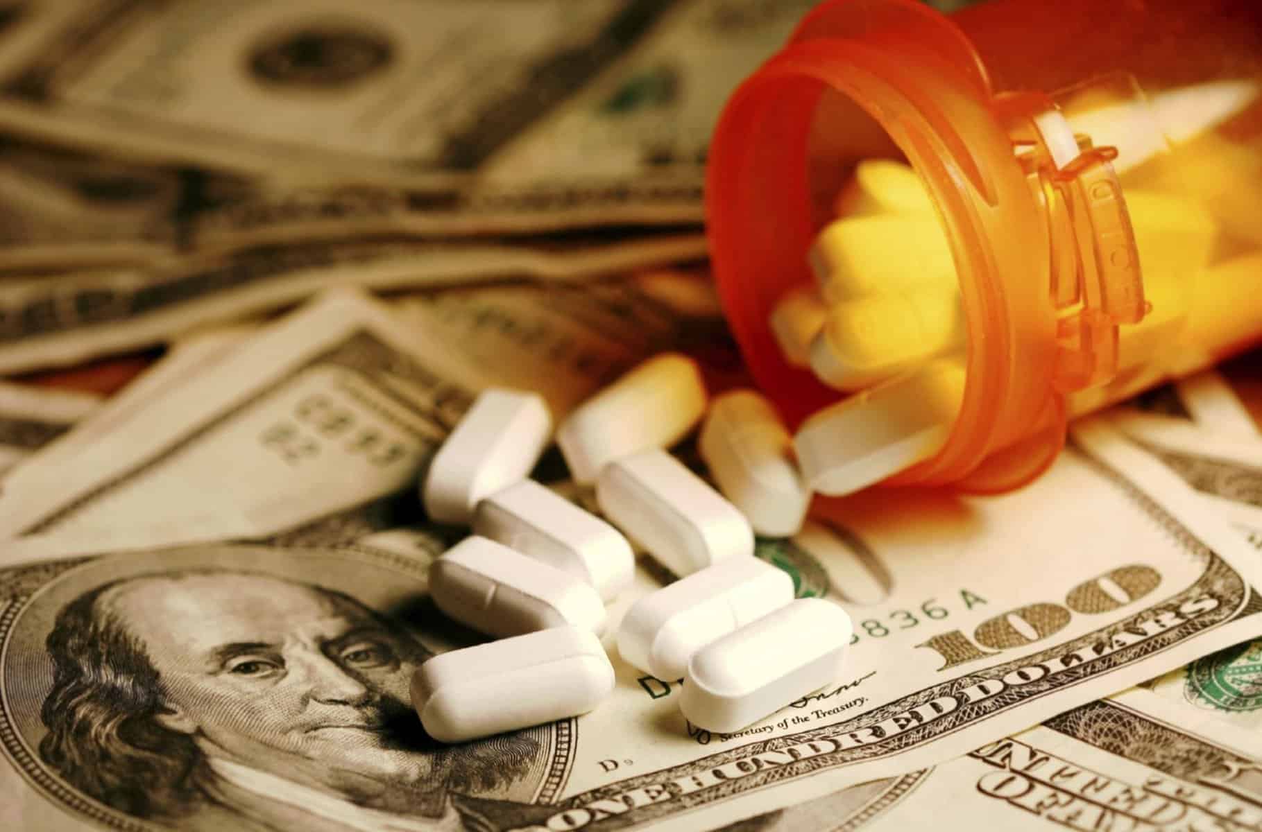 Prescription pills spilling out of a bottle onto $100 bills.
