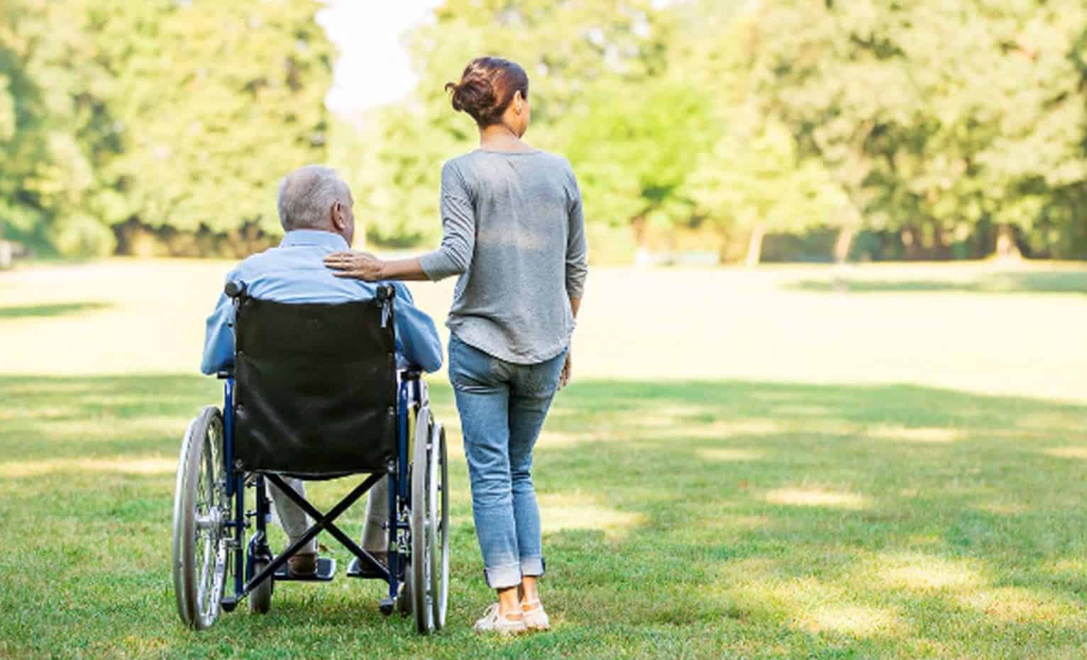 A woman standing next to an elderly man who is sitting in a wheelchair.